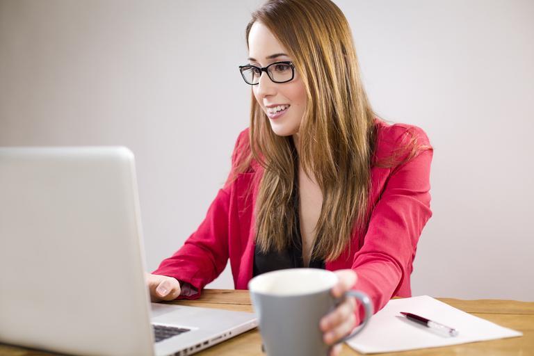 žena, která zpracovává něco na počítači a usmívá se, v klidu popíjí šálek třeba kávy
